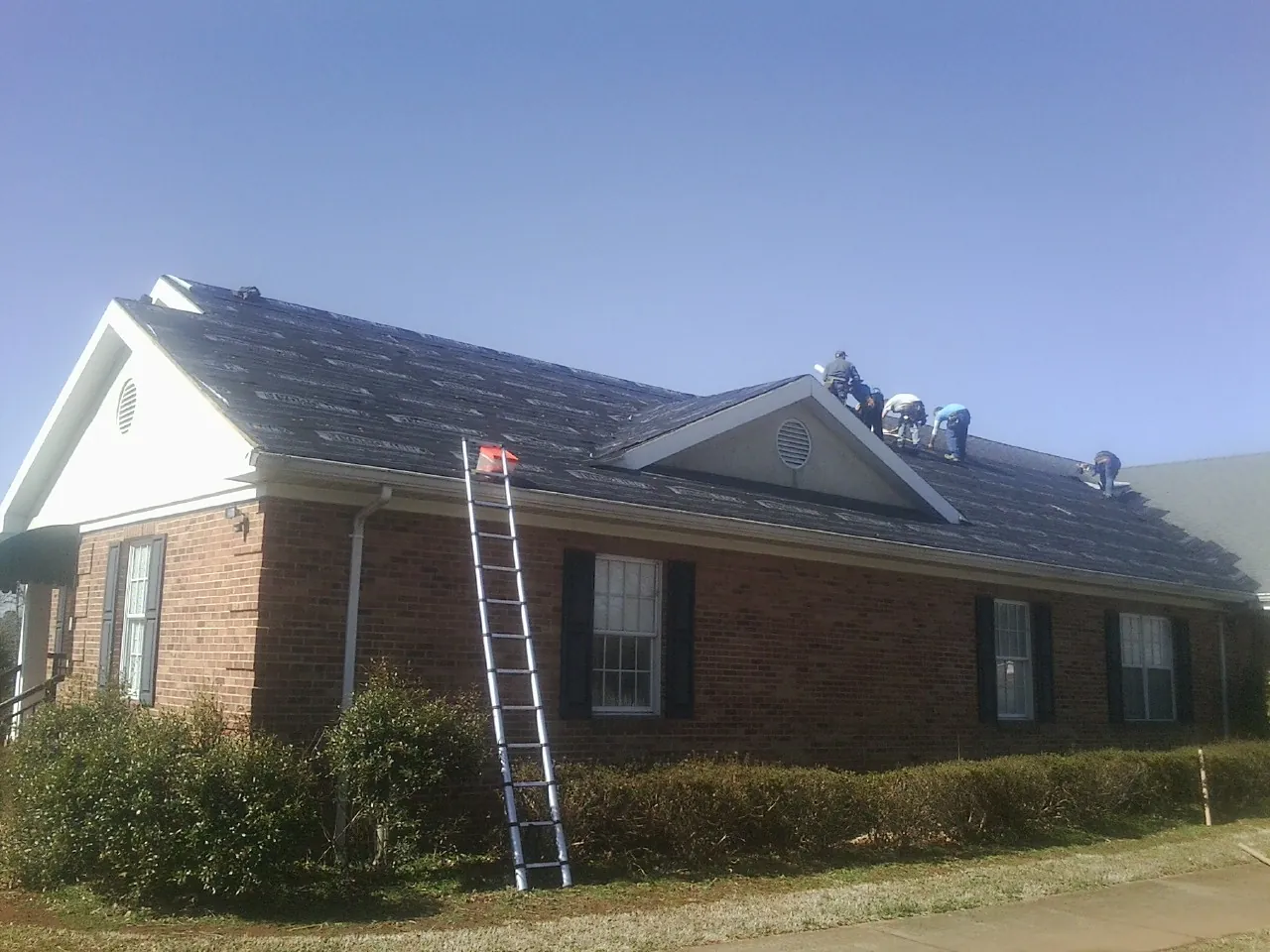 Crew tearing shingles off a brick ranch roof with a ladder set — Metal Roof Repair work by our crew in Sonyea