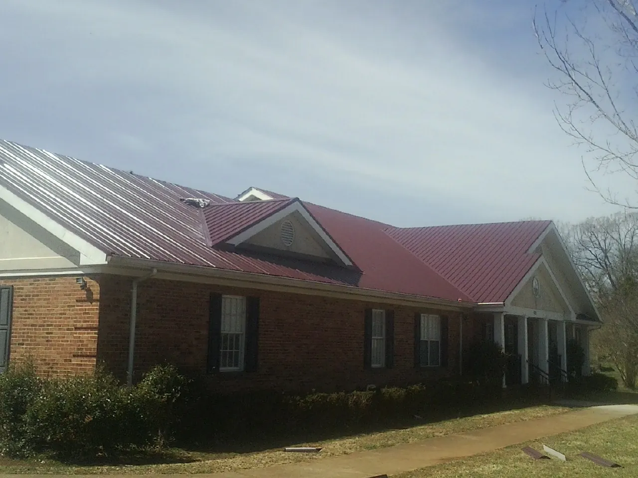 Red metal roof with gabled entries on a long brick building, from a Hail Damage Roof Repair job in Sonyea