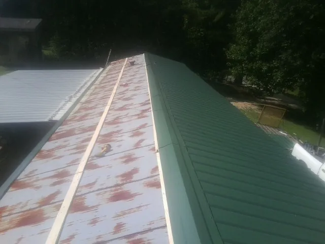 Old rusted panels beside newly installed green metal roofing — Wind Damage Roof Repair by Roofing Brothers in Sonyea