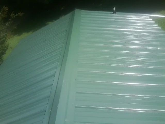 New green metal panels meeting at the ridge of a roof — Flat Roof Repair work by our crew in Sonyea