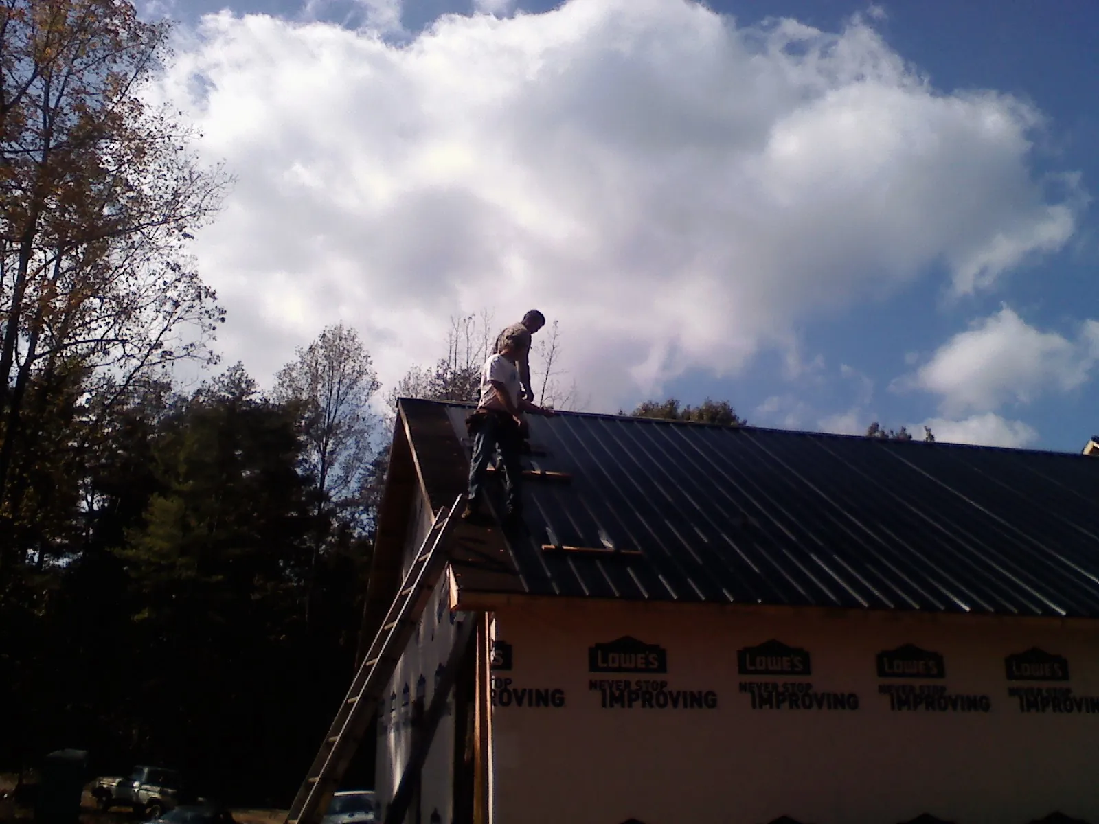 Roofer fastening dark metal panels high against a cloudy sky, from a Roof Inspection job in Sonyea