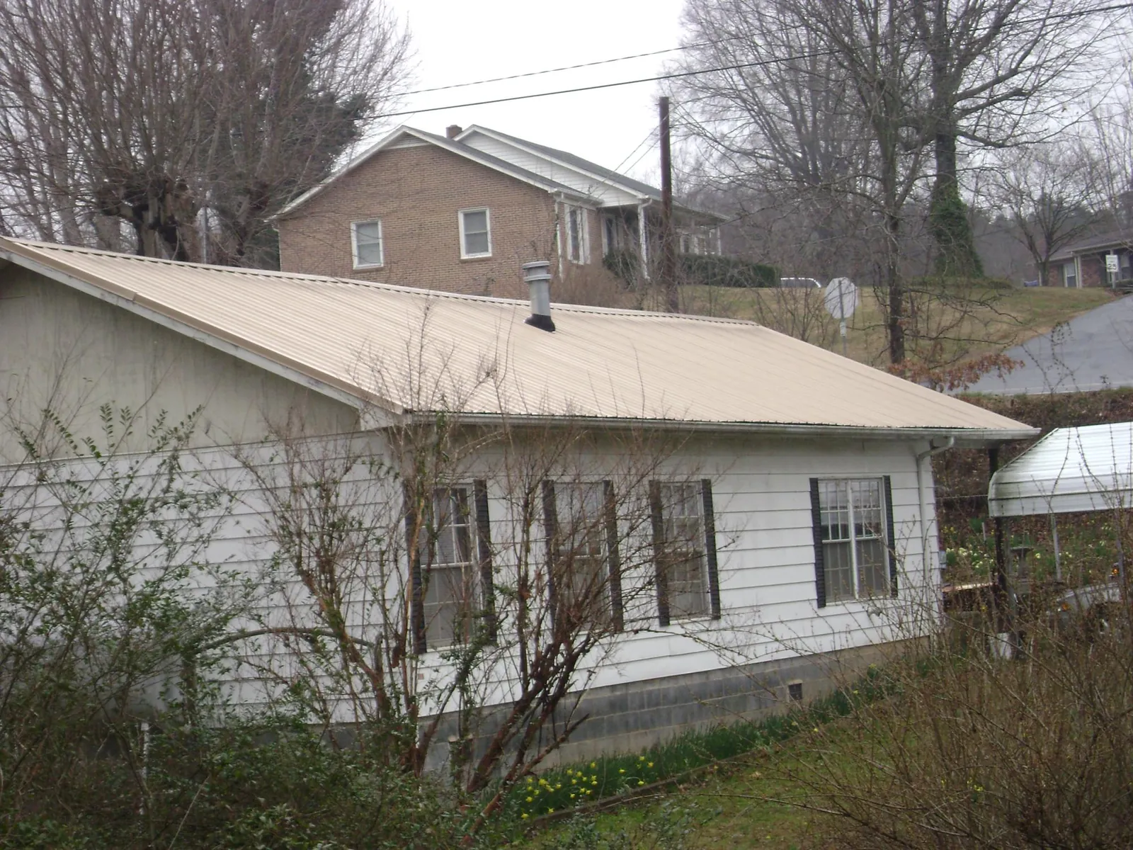 Tan metal roof on a white sided house set into a hillside — Commercial Roofing by Roofing Brothers in Sonyea