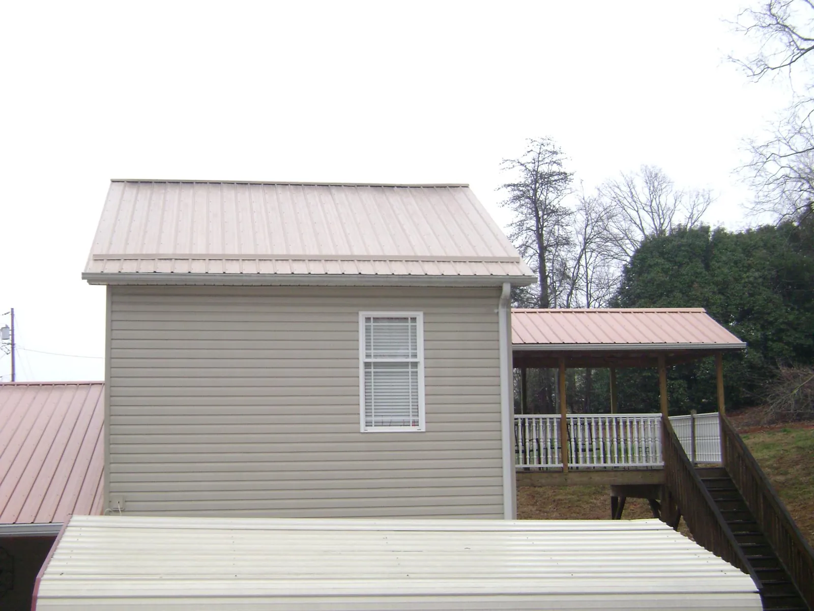 Tan metal roofs on a two story addition and attached porch, from a Roof Replacement job in Sonyea